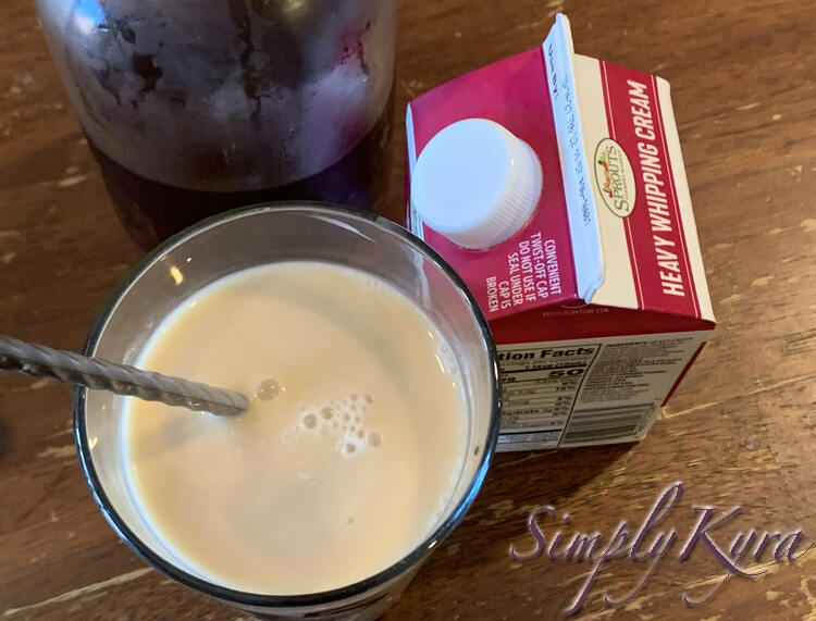 Image shows a stirred glass of white-brown liquid. To the right is a carton of heavy whipping cream and in the back is a half emptied canning jar of cold tea. 