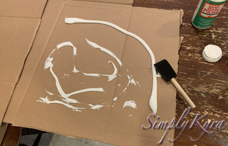 Image shows white goo in lines and smears on the cardboard with a foam brush sitting in on part. 