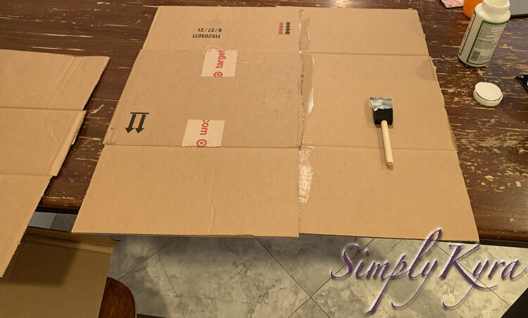 Image shows a large square of box composed of two Target box sections with a Mod Podge smeared foam brush on top of them. 