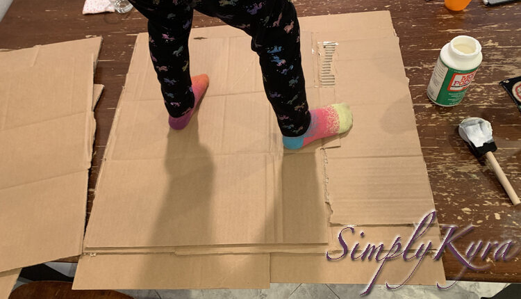 Image shows Zoey's lower half, with unicorn pants and bright sock, standing on the previous showing cardboard as if it was already a skateboard. 