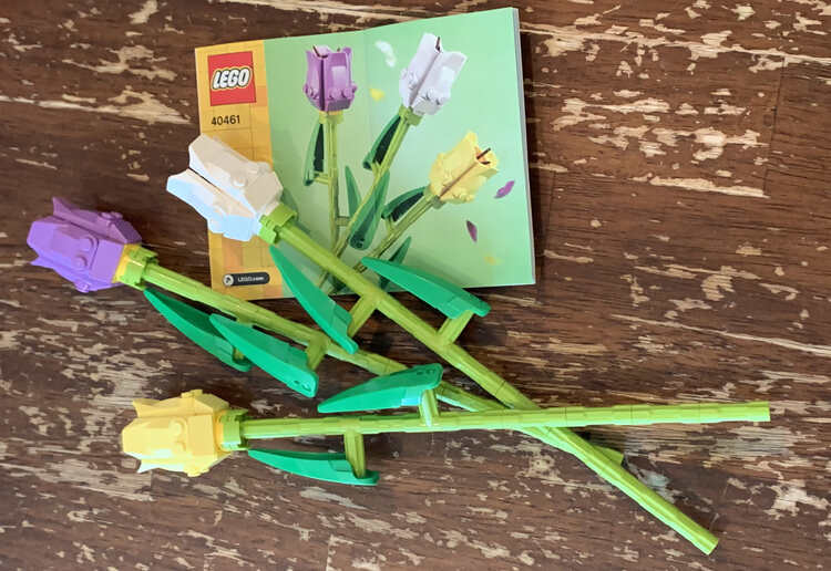 Image shows the three final tulips laid out on the table and tilted so the stems overlap under the leaves. The instruction book is below the white tulip with the lavender and then yellow tulip below. 