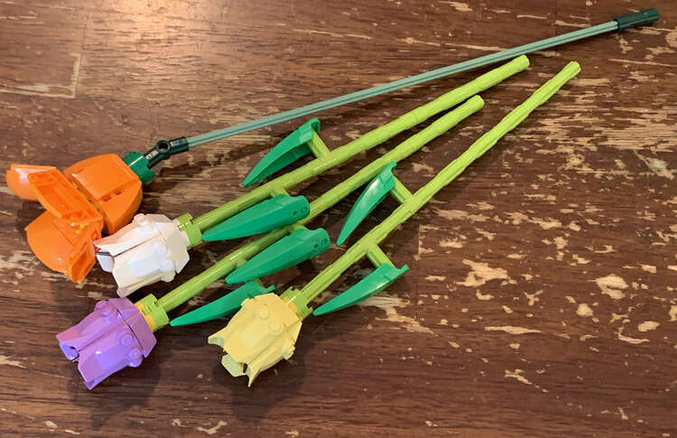 Image is taken from above looking down at the four tulips. The orange bloom is even-ish with the other three but it's stem extends past where the other ones end. 