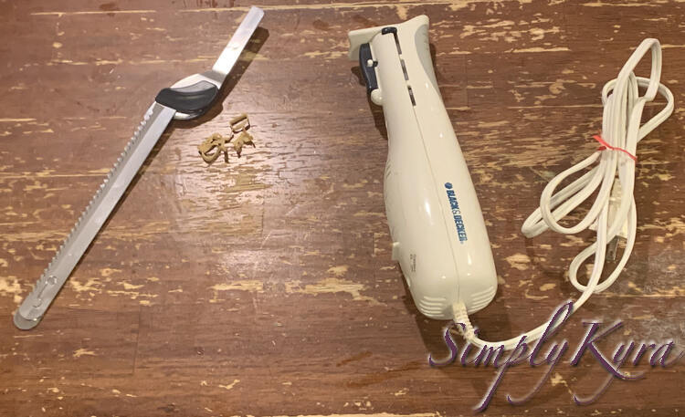 Image shows the electric knife base to the right with a red garbage tie keeping the electrical cord tied together. To the left lays the blades with a broken sad elastic between the two parts.  