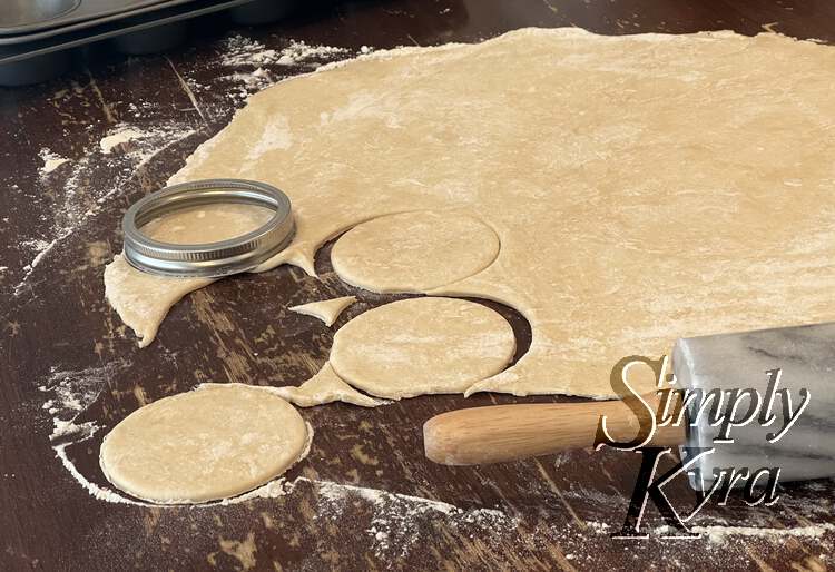 Image shows a smooth flat oval of pastry dough with four, almost five, circles cut out with a canning jar lid. My rolling pin sits off to the side. 