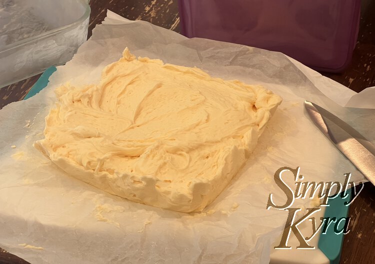 Image shows a square of solid yellow center with marks where a spatula attempted to flatten the top. It's sitting on parchment paper on a cutting board with a knife beside it. 