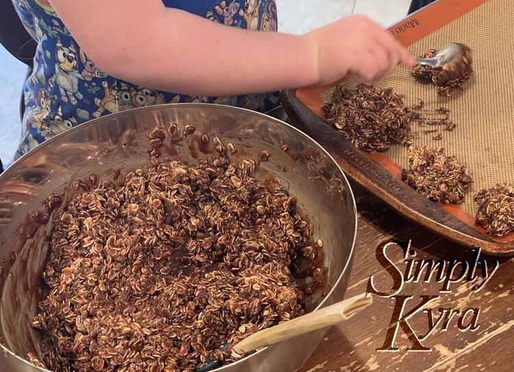 Image shows Ada's arm as she uses a spoon to make another cookie next to three others on a Silpat lined baking sheet. Beside it sits a metal bowl filled with the rest of the no-bake dough. 
