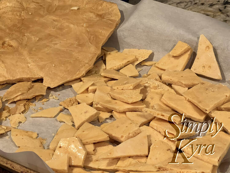 Image shows the parchment lined cookie sheet with light-colored broken honeycomb candy and a darker sheet resting to the side. 