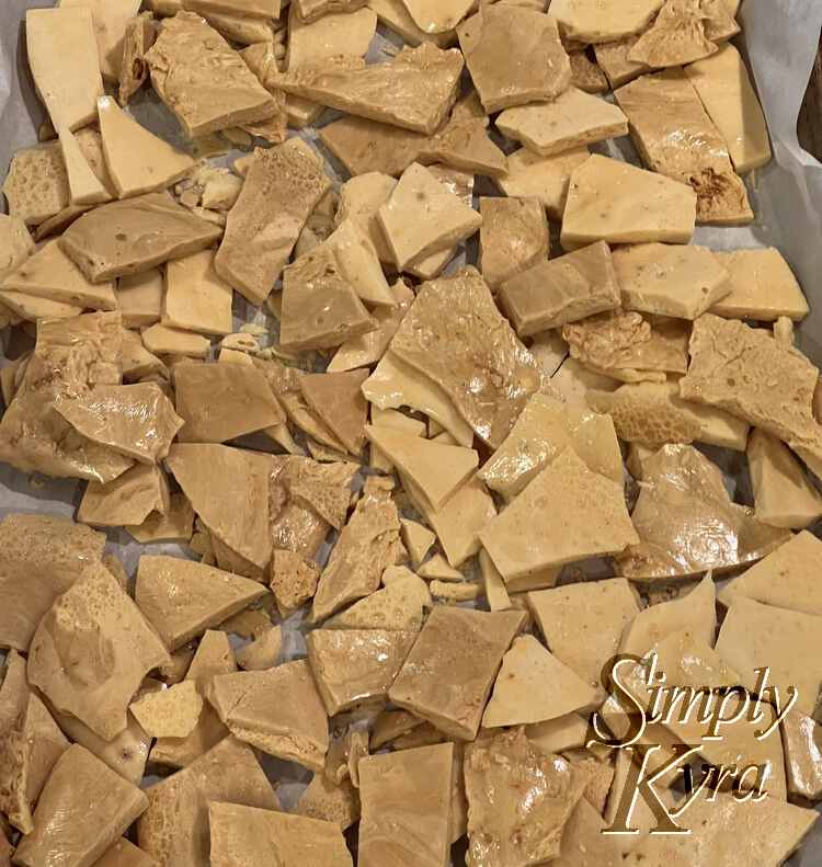Image shows a parchment lined cookie sheet full of sharp pieces of honeycomb candy in two shades. 