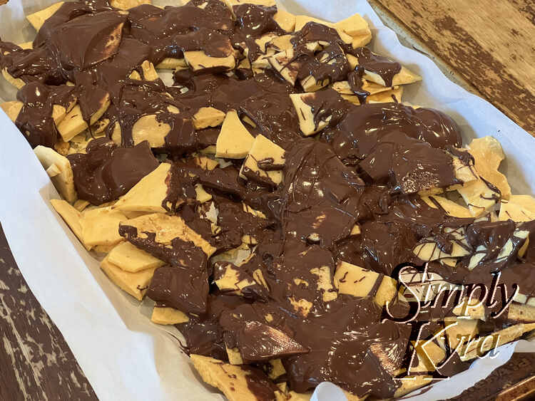 Image shows the parchment lined cookie sheet at an angle coated in broken up honeycomb candy with a solid drizzled chocolate overtop. 