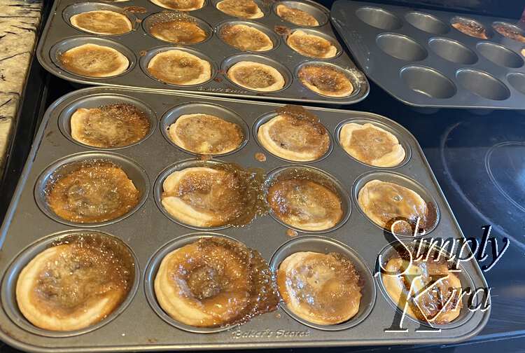 Image shows the three muffin tins resting on the oven top with browned, bubbled, tarts resting inside to col. 