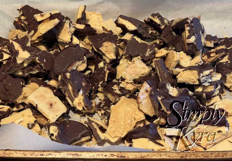 Image shows a mix of chocolate coated honeycomb candy in a pile on a parchment lined cookie sheet. 