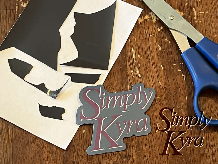 Image shows the SimplyKyra magnet trimmed so the backing is the same shape as the sticker. Behind it is the white sticker backing with pieces of the magnet still stuck to it. To the right are a pair of scissors.