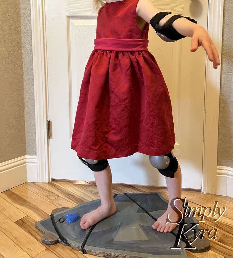 Now she stands on the skateboard with her knees bent and her arms out.