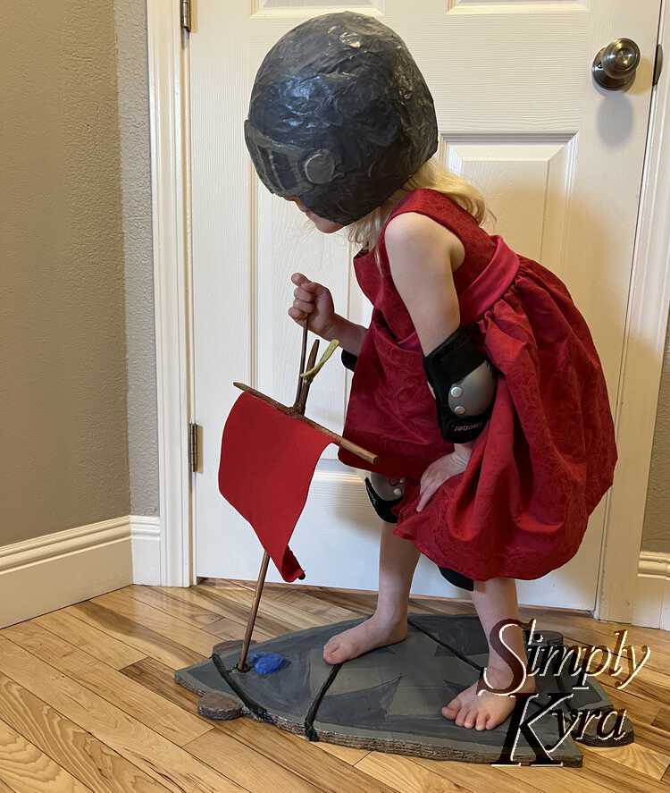 Same outfit and accessories as before but now she's standing with her knees bent. One hand is on the top of the mast keeping it in place while the other hand rests on her knee.