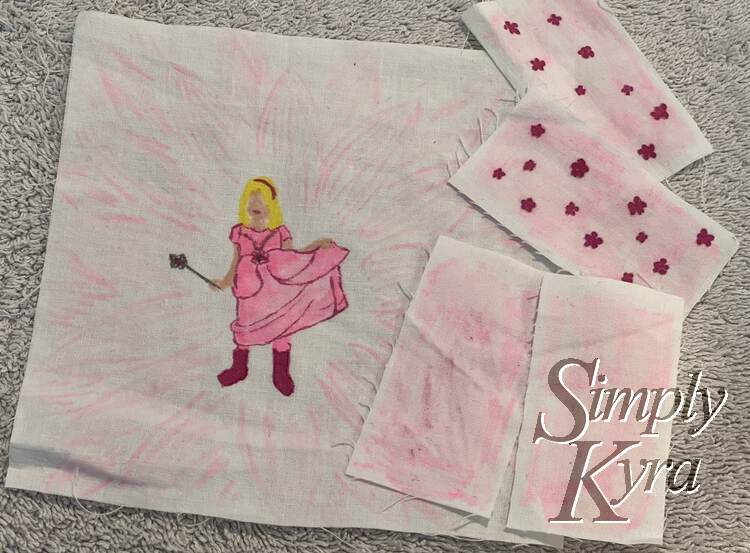 Image shows the square of fabric with Ada's silhouette drawn on. There are four small rectangles to the side. Both are shaded in light pink while two of them have dark pink flowers to match Ada's boots and dress outline. 