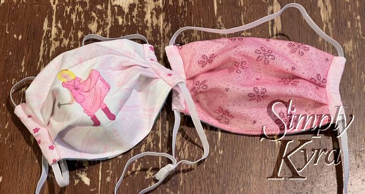 Image shows two finished masks side by side. The one with the silhouette and flowered edges is to the left and the sparkly tulle one with the pink edges is to the right.
