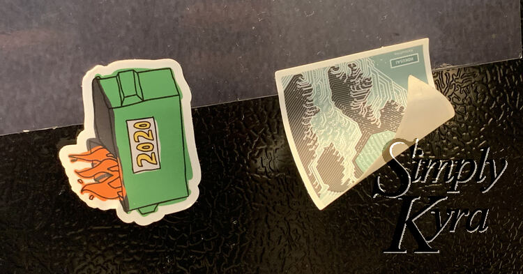 Image shows two stickers attached to the grey magnetic sheet on my fridge. The one sticker is thicker and flat while the other one is curling up showing it's only attached at the top.