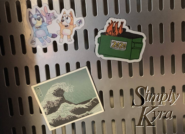 The image shows the metal pegboard with the Bluey and dumpster fire magnets at the top and the circuit board art magnet at the bottom center.