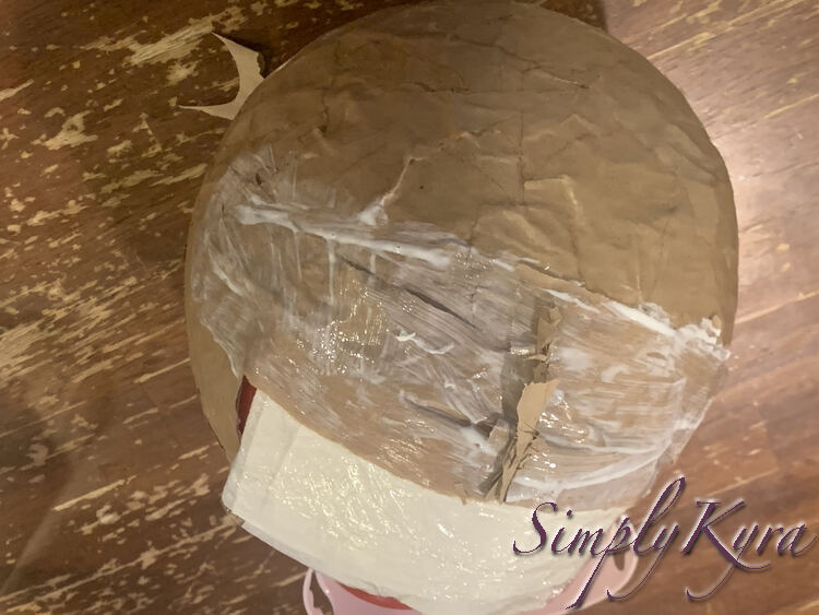 Image shows the center top of the helmet with the white glossy paper towel sticking out below the visor. The visor itself is streaked in white with unrolling pieces of brown paper vertical lined up in the center. 