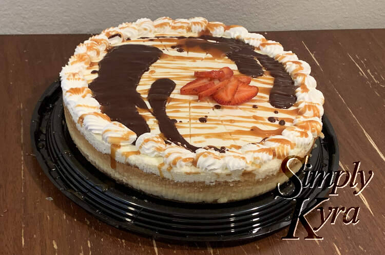 Image shows the final chocolate, caramel, and strawberry festooned cheesecake taken from above and to the side.