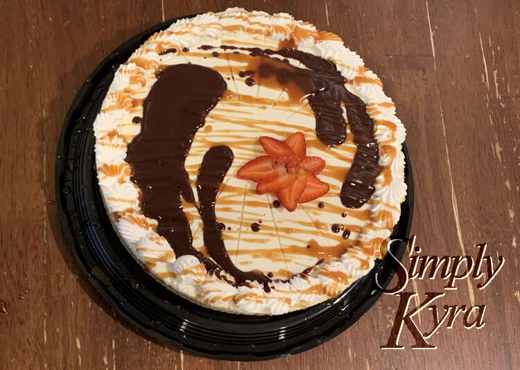 Image is taken from above looking down at the cheesecake drizzled in caramel, dolloped with chocolate, and with a strawberry slice flower near the center. 