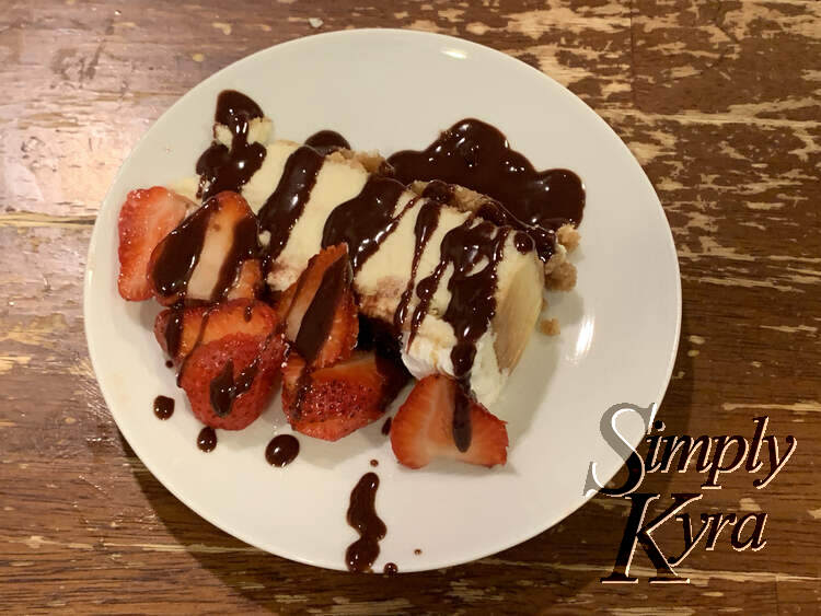 The slice is on its side with the sliced strawberries laying beside it as if it was topped with them. There are drizzles of chocolate sauce crisscrossing the length of it going from top to bottom and back again.