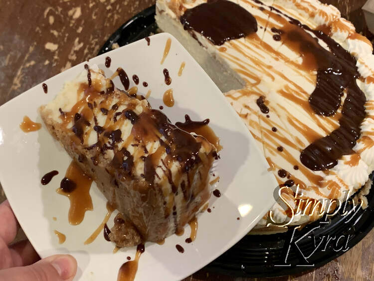 Image shows a slice of cheesecake on its side on a square white saucer. There are light and dark brown dollops all over it make it look arty. Behind the saucer you can see the rest of the bedazzled cheesecake.