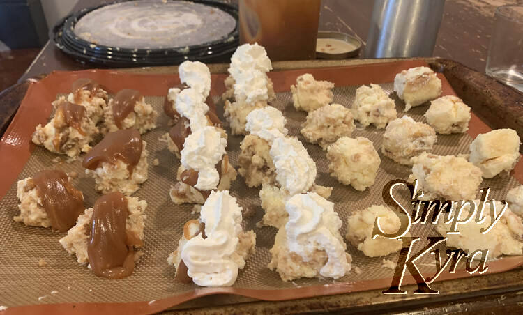 Image shows seven lines of cheesecake balls laid out across the cookie sheet. The six leftmost ones are topped with caramel while the nine ones beside it are topped with whipped cream.