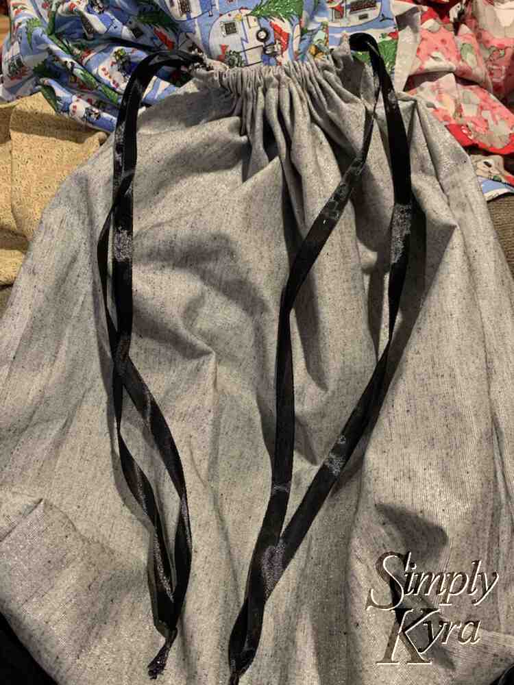 Image shows the same silver bag this time cinched closed with a loop of black ribbon coming out of either side. The rest of the bags are blurred slightly in the background. 