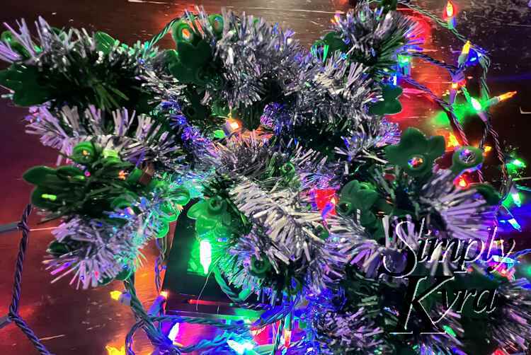 Image shows a closeup view of the lit up tinsel on the bonsai from above with the lights surrounding the base below. 