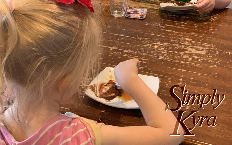 Image shows the back of Zoey's head as she uses a spoon to taste the sauce. In the background you can see Ada's hand tilting her saucer as she does her own tasting. 