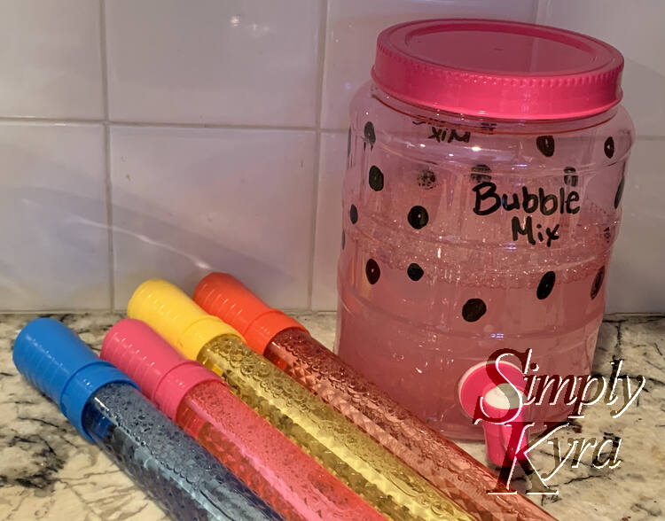 Image shows a pink plastic drink dispenser with bubbly liquid inside and the words "Bubble Mix" and bubbles written on the outside. There are bubble wands to the side. 