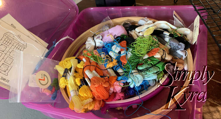 Image shows an opened pink square container filled with open circles and many colors of thread. 