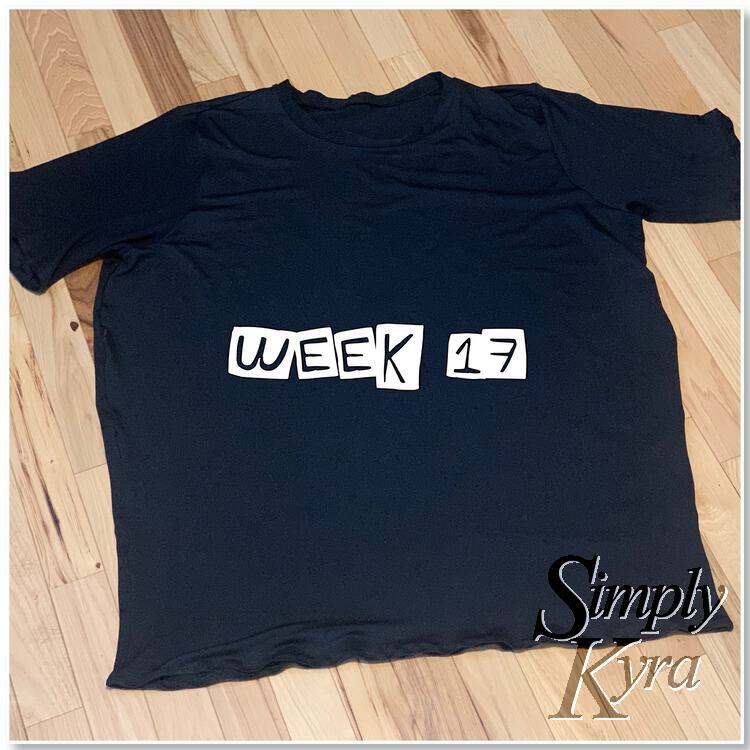 Image shows a plain black tee laid out on the floor with the words, in white, laid overtop saying "week 17".