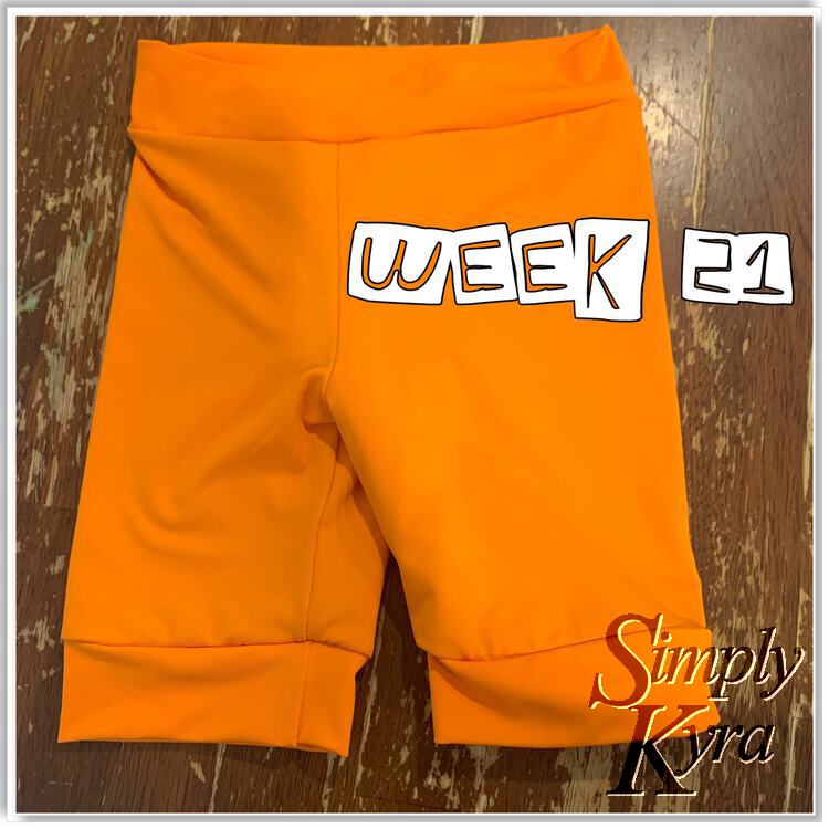 Single image showing a pair of orange swim shorts with the words "week 21" overlaid overtop. 