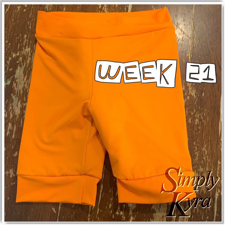 Single image showing a pair of orange swim shorts with the words "week 21" overlaid overtop.