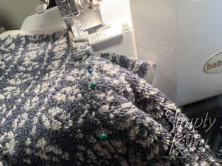 Image shows the towel under the pressure foot with about two inches already cut into the center. The green and blue sewing pins lead away from the pressure foot towards the edge of the photo.