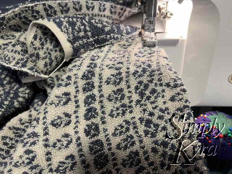 Image shows the second side being serged with its beginning corner still connect, via the rolled hem stitch, to the other half.