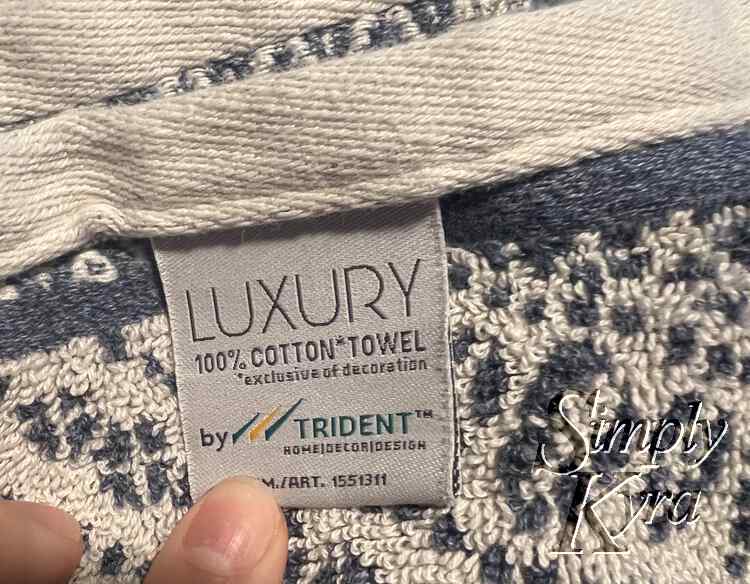 Closeup image of the tag for the new towel. It says Luxury 100% cotton towel by Trident home|decor|design.
