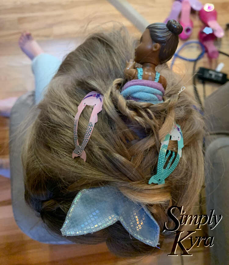 Image taken from above looking down at the top of Ada's head showing how the doll is kept in. You can see a looped floral wire end sticking out from a thin braid wrapped around the doll. The lower half is braided in and there's two mermaid clips on either side. 