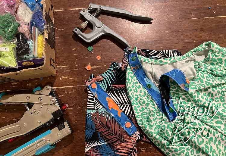 Image shows the two plackets with one open and the other snapped closed. There's also a box of bagged KamSnaps, the Crop-o-Dile II, the KamSnap tool, and three broken leftover KamSnap pieces. 
