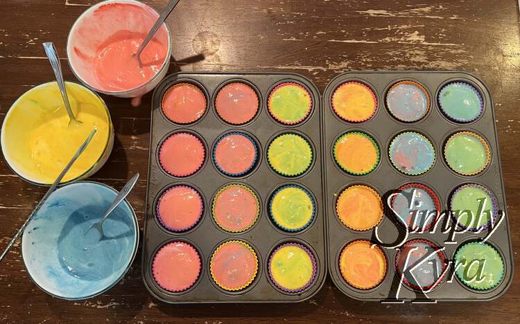 Image shows the two cupcake tins with, from left to right, columns of orange, purple, green, orange, purple, and green. The same three bowls with red, yellow, and blue are off to the left. 