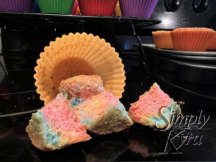 Image shows a cupcake cut into four pieces and spilling from an orange silicon liner. You can see the rest behind it on the cooling rack and cupcake tin.