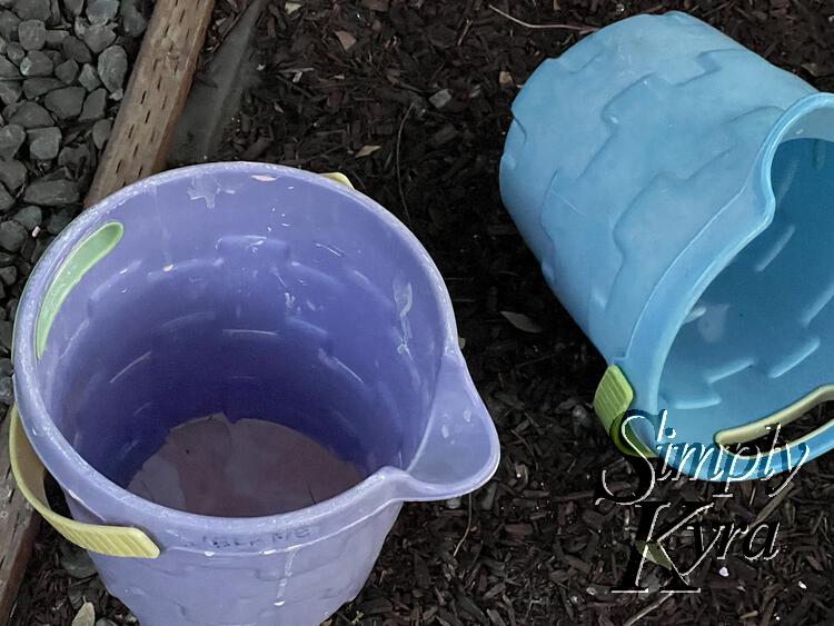 Image shows two buckets. The one on the left has pink oobleck at the bottom. The blue one on the right is tipped over and you can't see if it's clean or not.