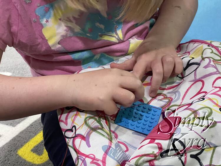 Ada is bent over her backpack and she's stitching the patch to the front. The thread is creating dashes along the side of the patch.
