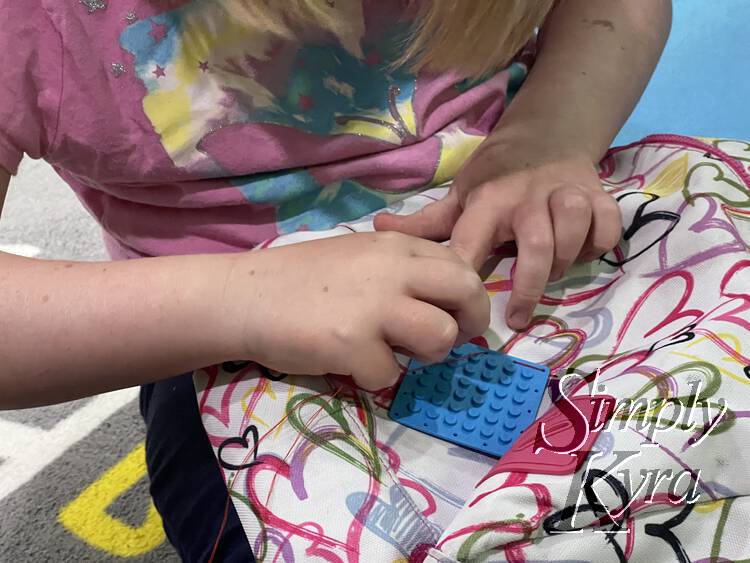 Ada is bent over her backpack and she's stitching the patch to the front. The thread is creating dashes along the side of the patch. 