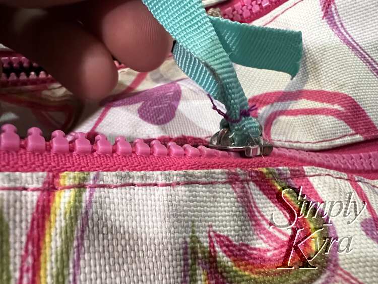 Image shows a closeup of one of the teal ribboned zipper pulls but now there's clear hot glue around the base. 