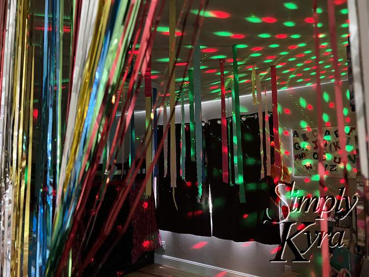 Image shows the metallic streamers pulled back like a curtain showing up the multicolor crepe streamers hanging from the ceiling and the red and green lights projected everywhere. 