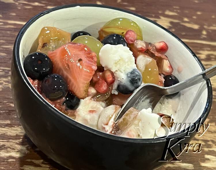Image shows a small black outer bowl with ice cream and fruit salad (grapes, strawberries, and pomegranate seeds). 
