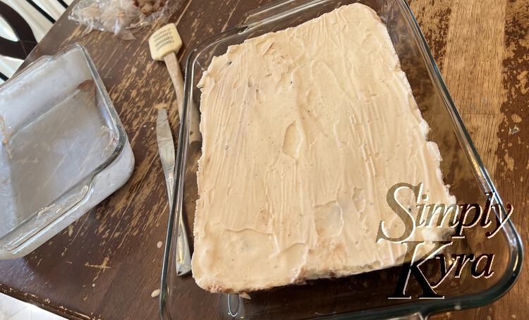 Image shows the cake in a larger dish with the dirtied spatula, butter knife, casserole dish, and plastic wrap in the back. 